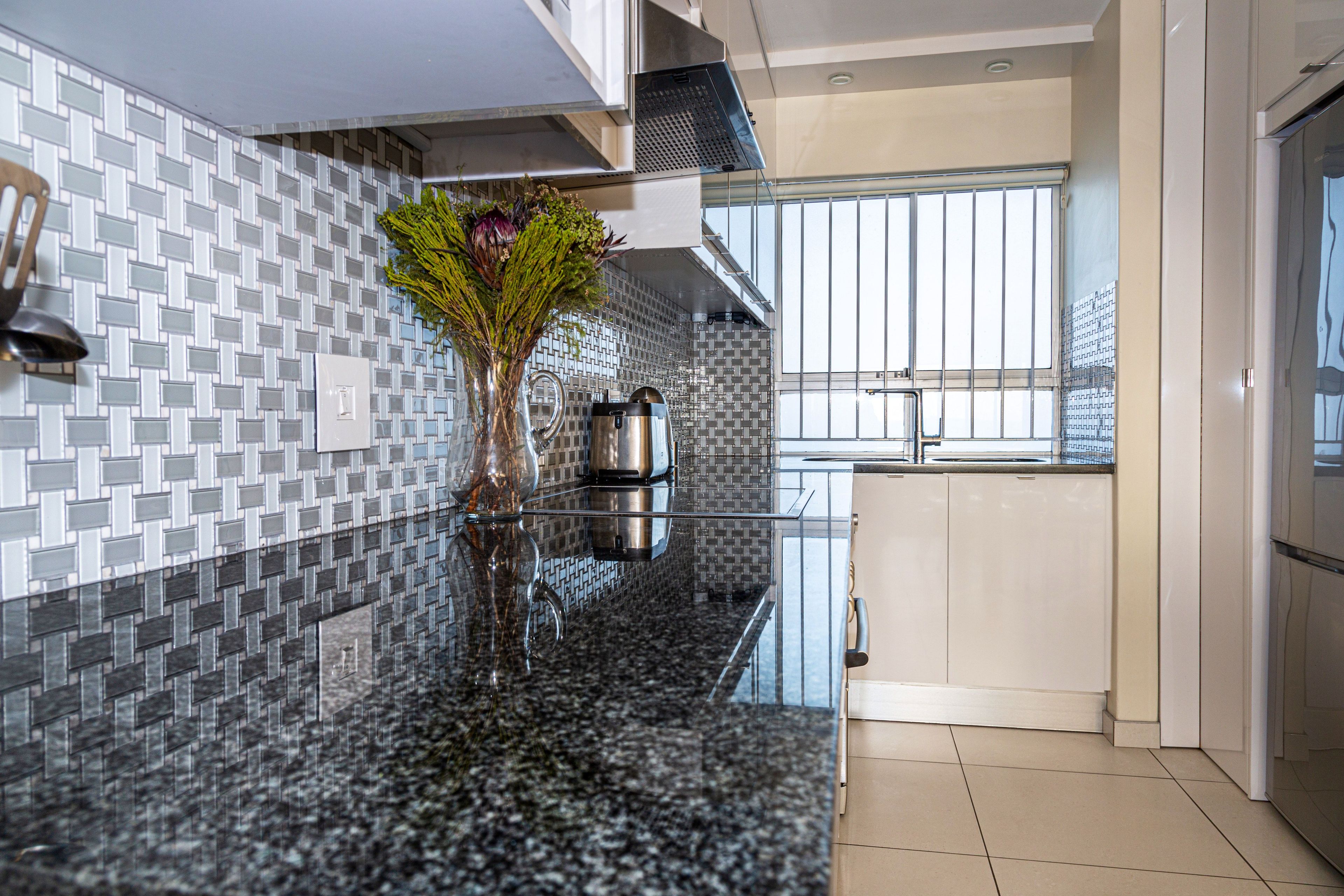 A modern kitchen with a granite countertop, a stainless steel kettle, and a vase with flowers.