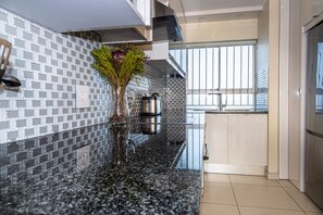 A modern kitchen with a granite countertop, a stainless steel kettle, and a vase with flowers. - Sea Spray A308 (Cape Town)