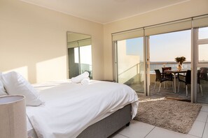 A bedroom with a bed, a large window, and a balcony with a table and chairs. - Sea Spray A308 (Cape Town)