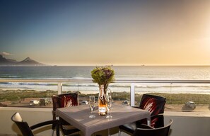 A table with a bottle and two glasses, overlooking a beach and ocean. - Sea Spray A308 (Cape Town)