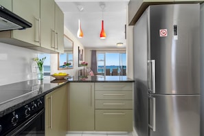 A modern kitchen with a stainless steel refrigerator, a stove, and a dining area with a view.