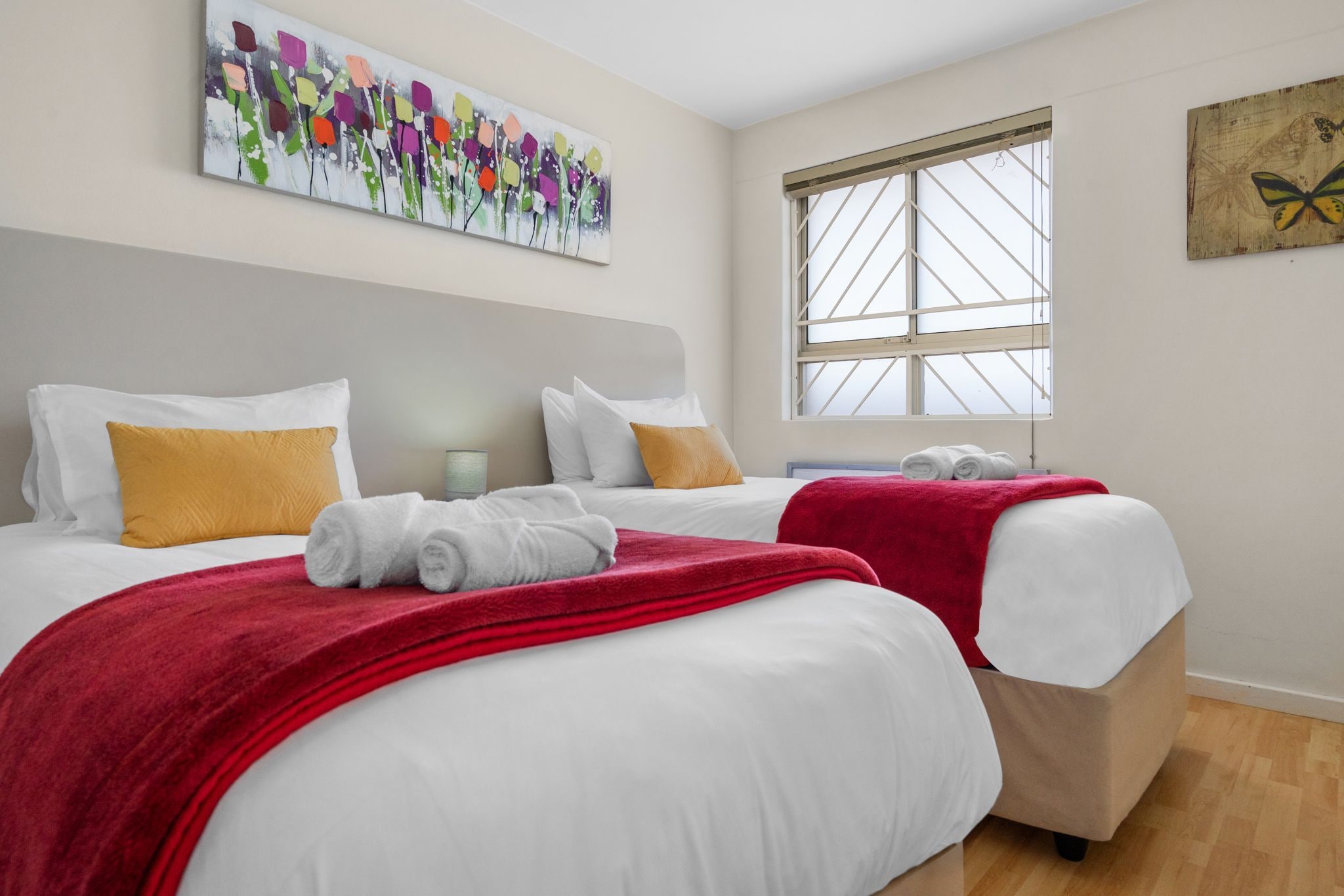 Habitació d'hotel amb dos llits, roba de llit blanca, almoinades vermelles i grogues, una manta vermella i obra d'art a les parets.
