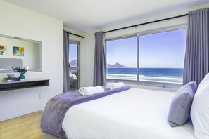 A modern hotel room with a large bed, a view of the ocean, and a balcony with a scenic mountain view. - Sea Spray B306 (Cape Town)