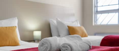 Una cama bien hecha con ropa de cama blanca y roja, una manta roja y almohadas en amarillo y blanco.