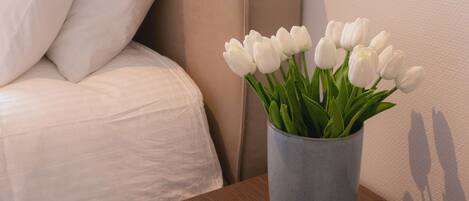 Ein Hotelzimmer mit einem Bett, einem Nachttisch, einer weißen Tasse und einer Vase mit weißen Tulpen.