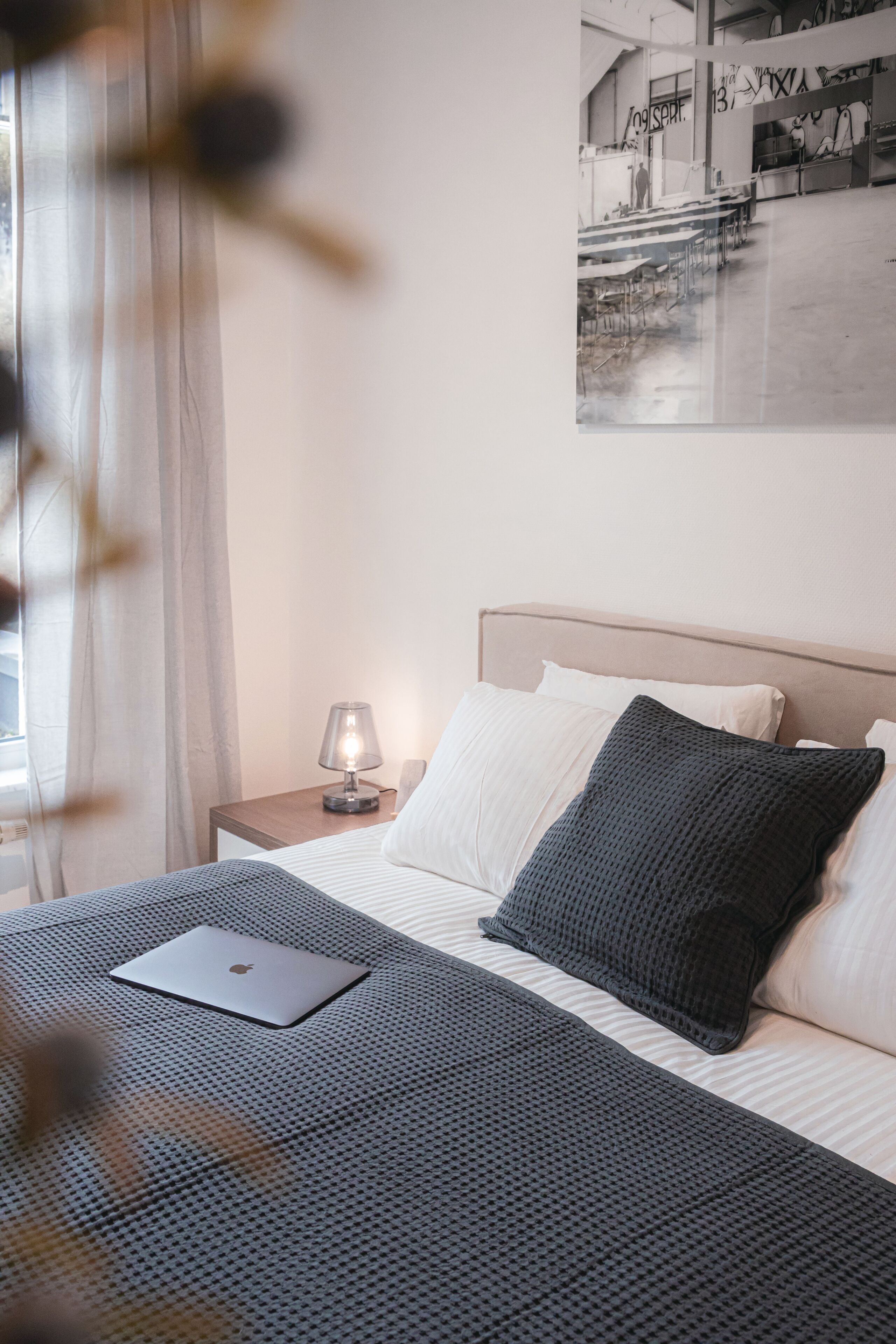 A neatly made bed with a laptop, a bedside lamp, and a framed picture on the wall.