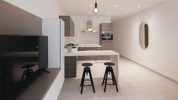 A modern kitchen with a central island, two bar stools, a built-in oven, and a large mirror on the wall.