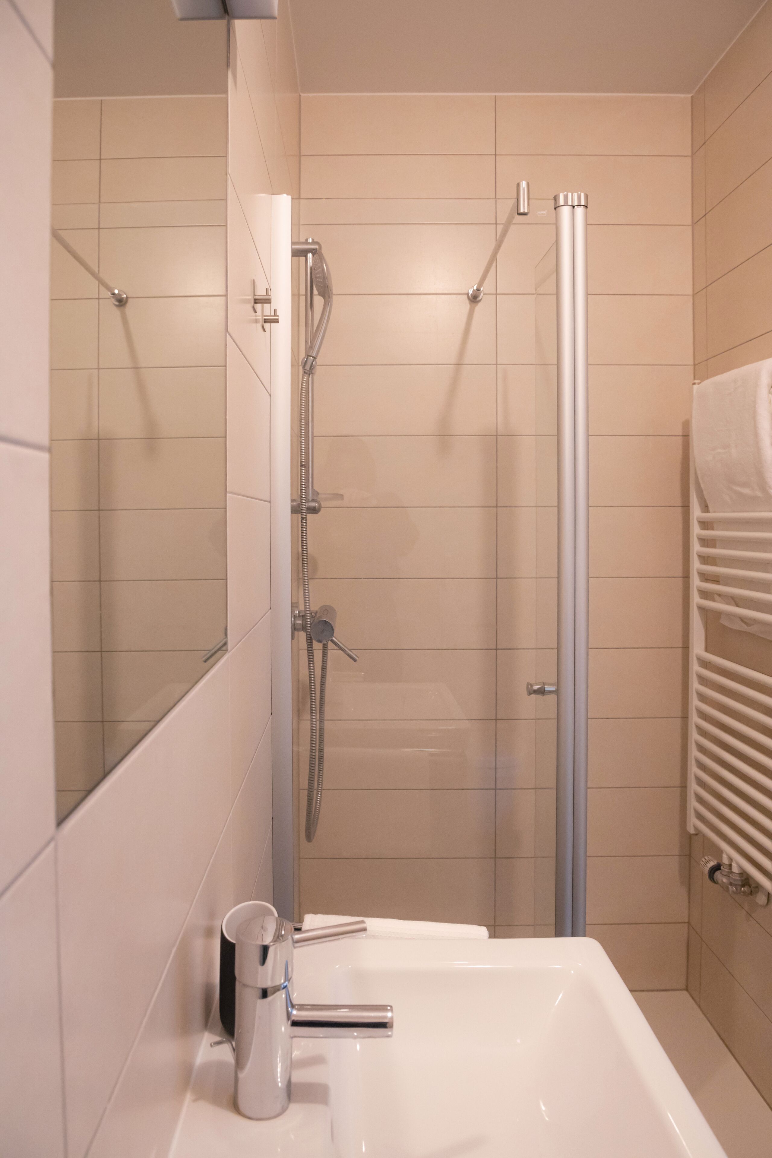A modern bathroom with a glass-enclosed shower, a white sink, and a towel rack.
