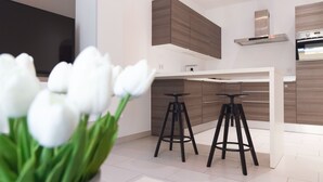 A modern kitchen with wooden cabinets, a stainless steel range hood, and two black bar stools.