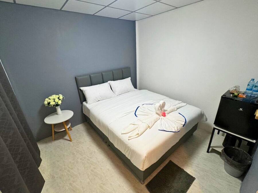 Un lit bien fait, agrémenté d’une décoration réalisée avec des serviettes, une petite table ronde sur laquelle est posé un vase de fleurs, et un meuble noir sur lequel sont disposés divers objets.