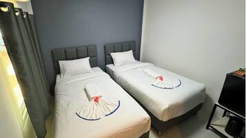 A hotel room with two single beds, a flat-screen TV, and a small kitchenette.