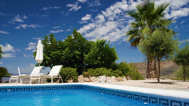 A clear blue swimming pool with white lounge chairs and an umbrella, surrounded by greenery and a rocky landscape. - Boutique B&B El Refugio (Alcaucin)