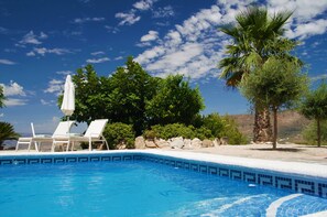 A clear blue swimming pool with white lounge chairs and an umbrella, surrounded by greenery and a rocky landscape. - Boutique B&B El Refugio (Alcaucin)