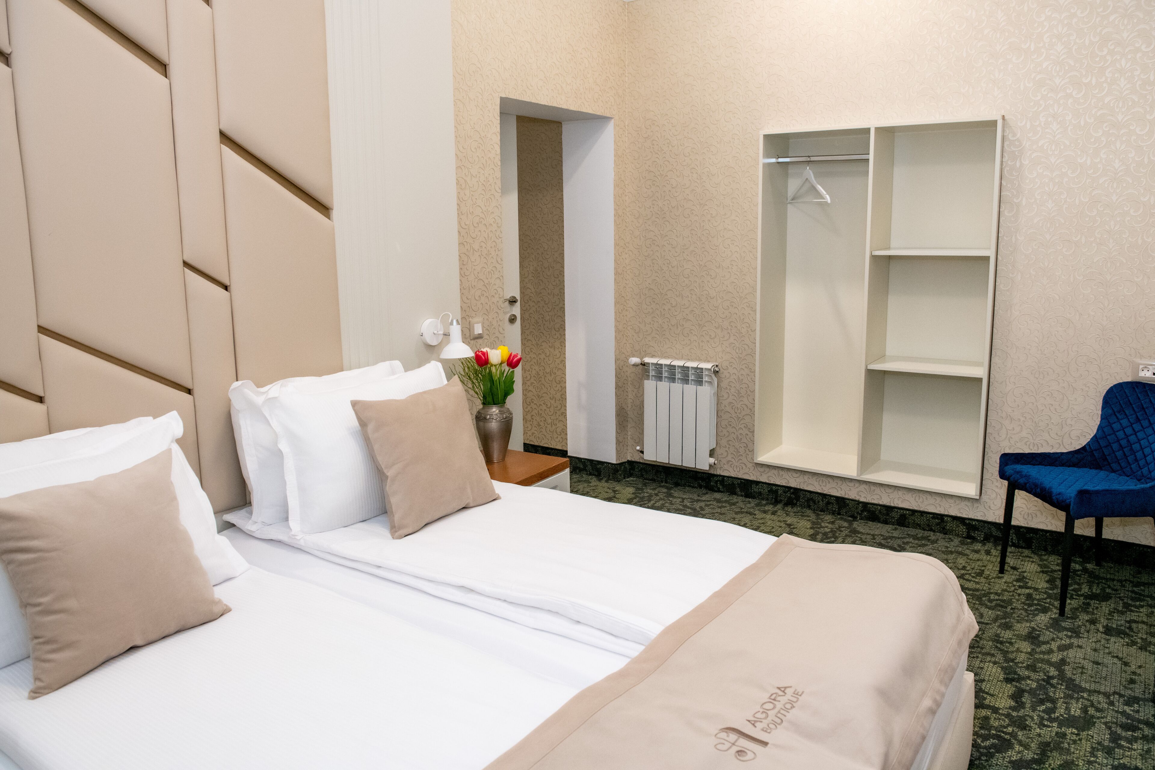 Una habitación de hotel con cama, una silla, un armario y una mesita con un jarrón de flores.