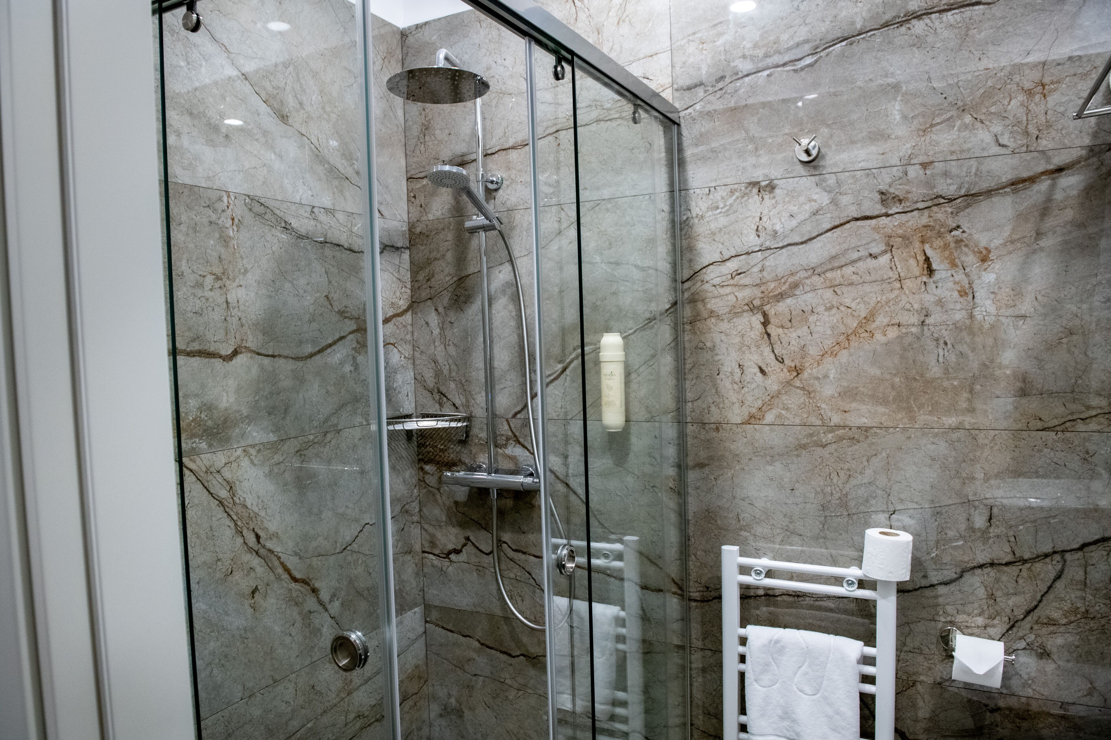 A glass-enclosed shower with a handheld showerhead, a glass door, and a towel rack with a towel.