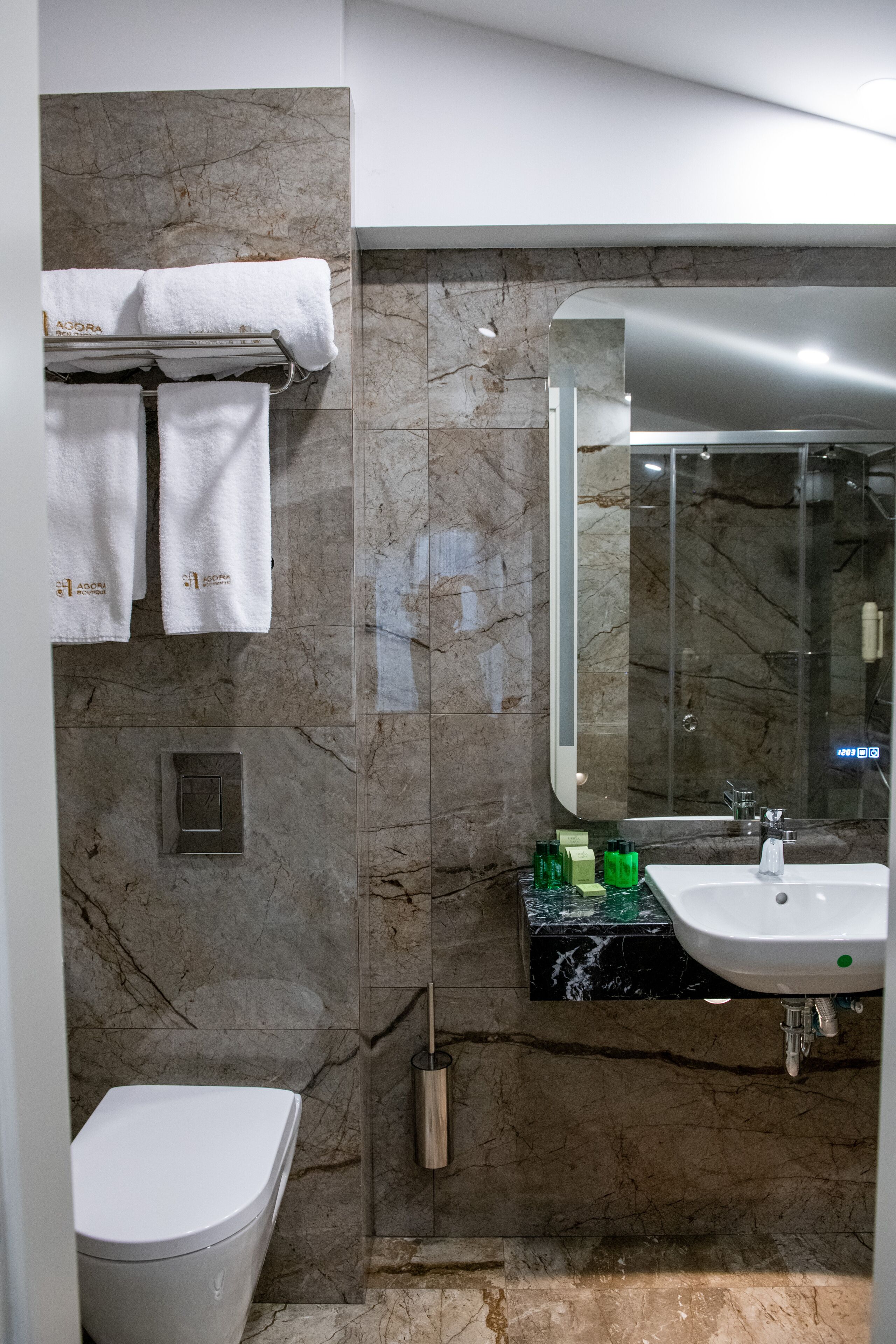 A modern bathroom with a marble wall, a toilet, a sink, and a mirror.
