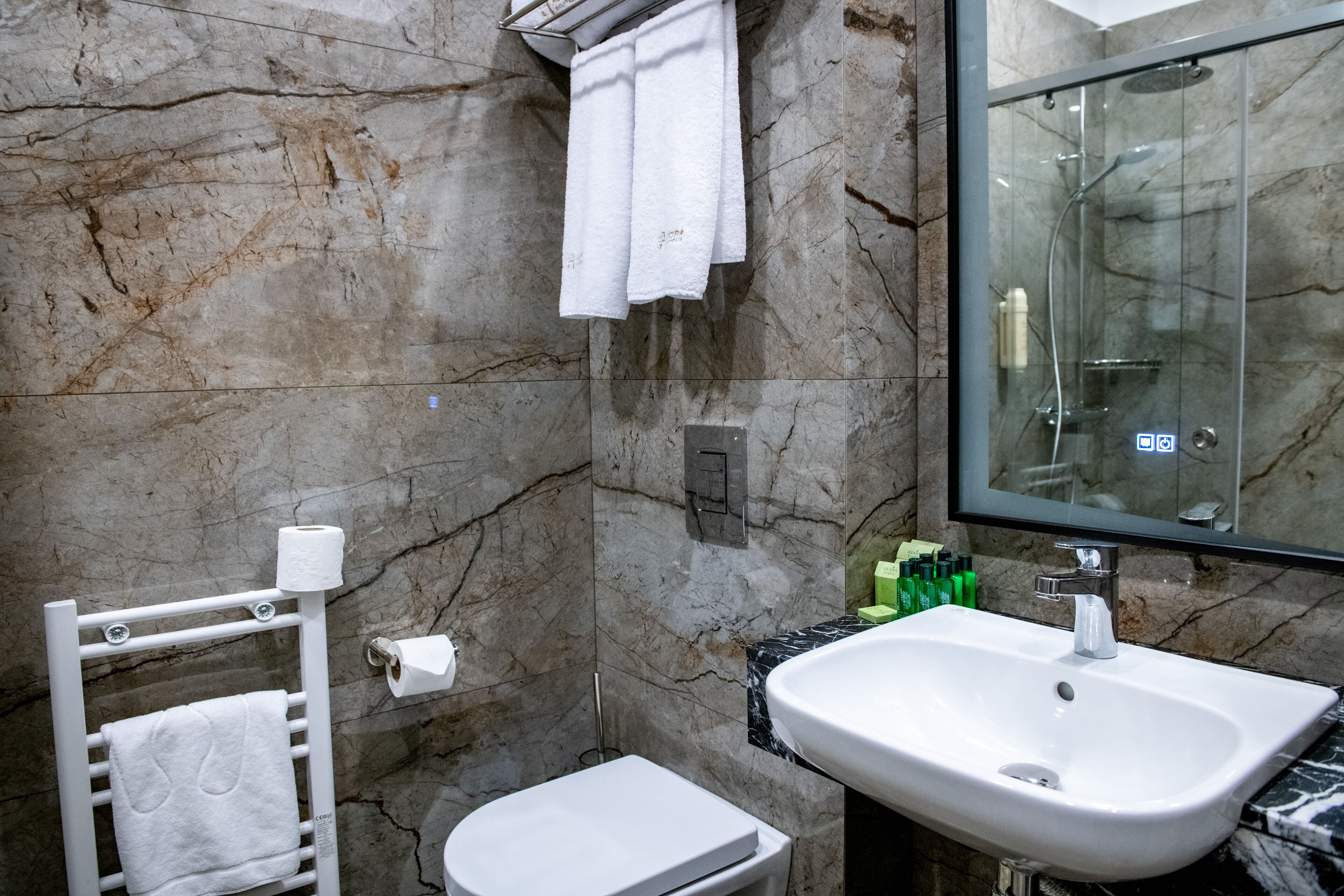 A bathroom with a marble wall, a white sink, a glass shower enclosure, and a towel rack.