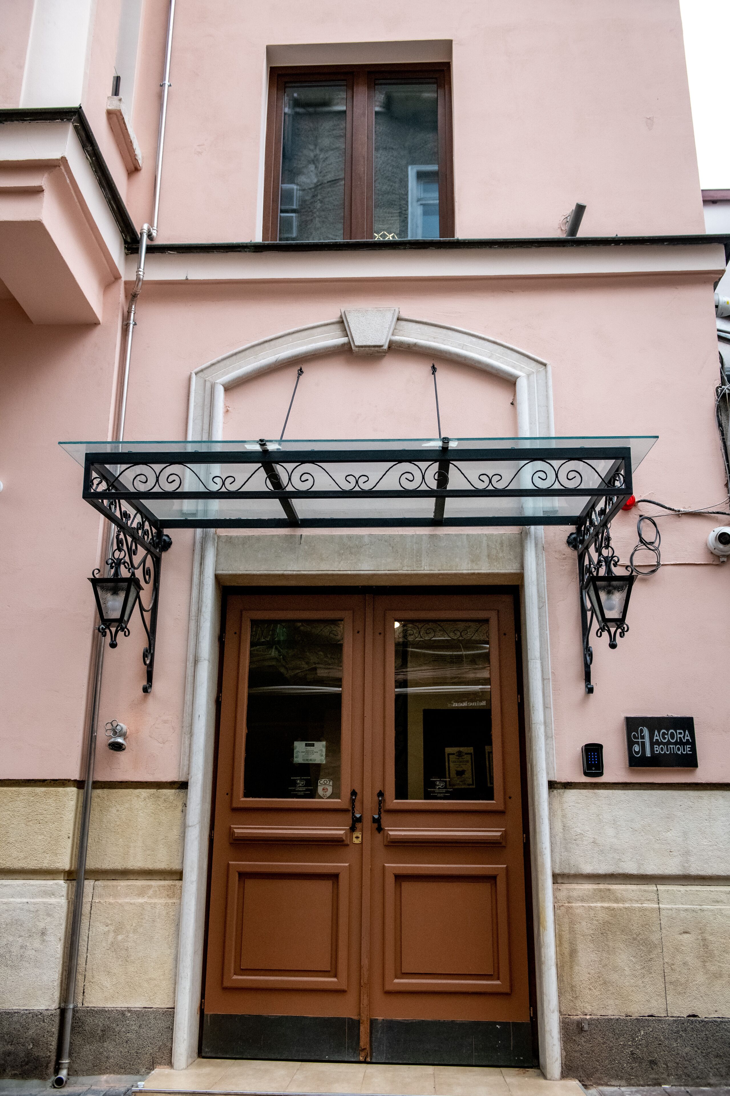 A double wooden door with a glass panel, a metal awning above, and a sign for "Agora Boutique" on the building's facade.