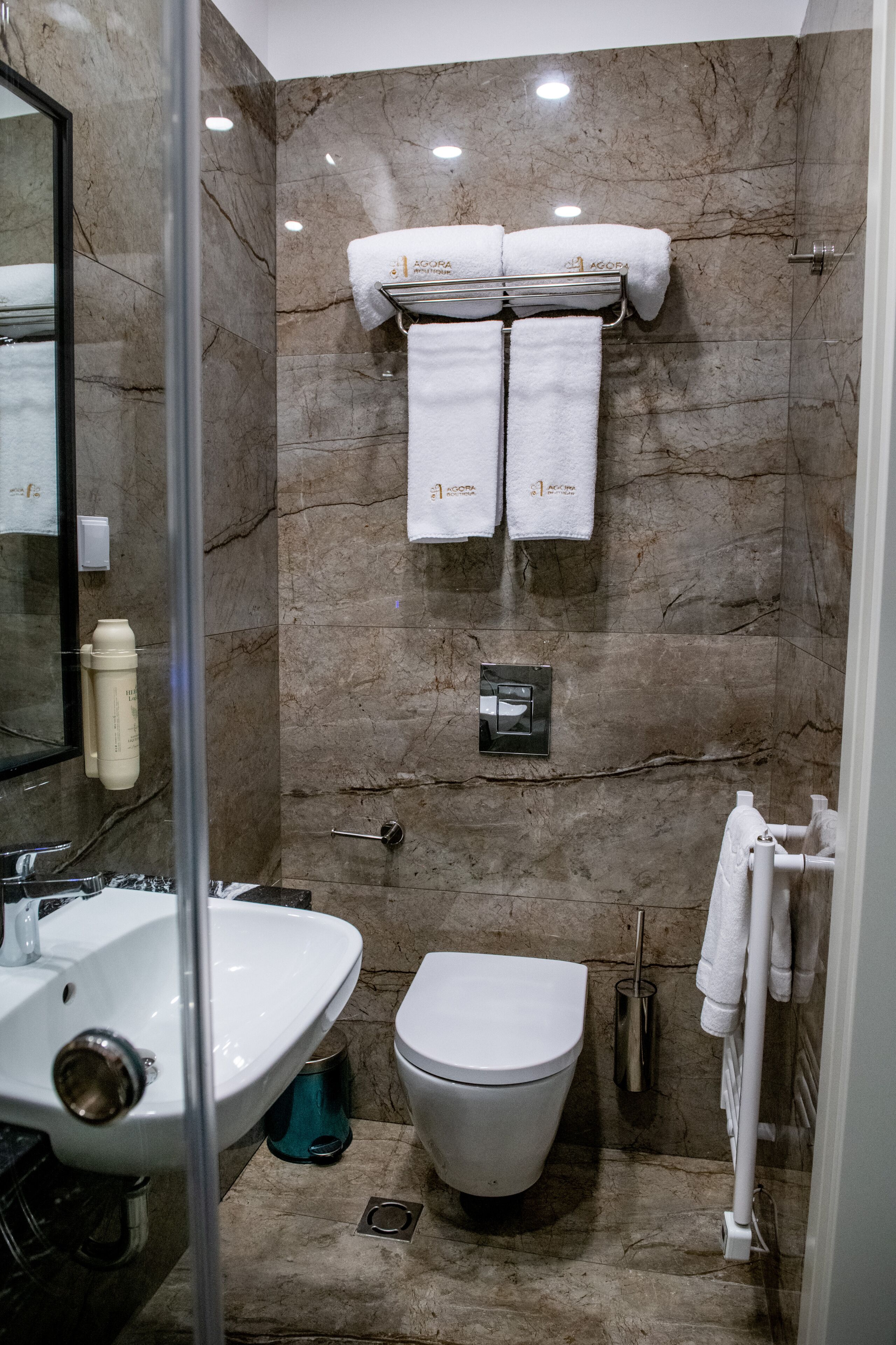 A modern bathroom with a marble wall, a glass shower enclosure, a white sink, and a toilet.