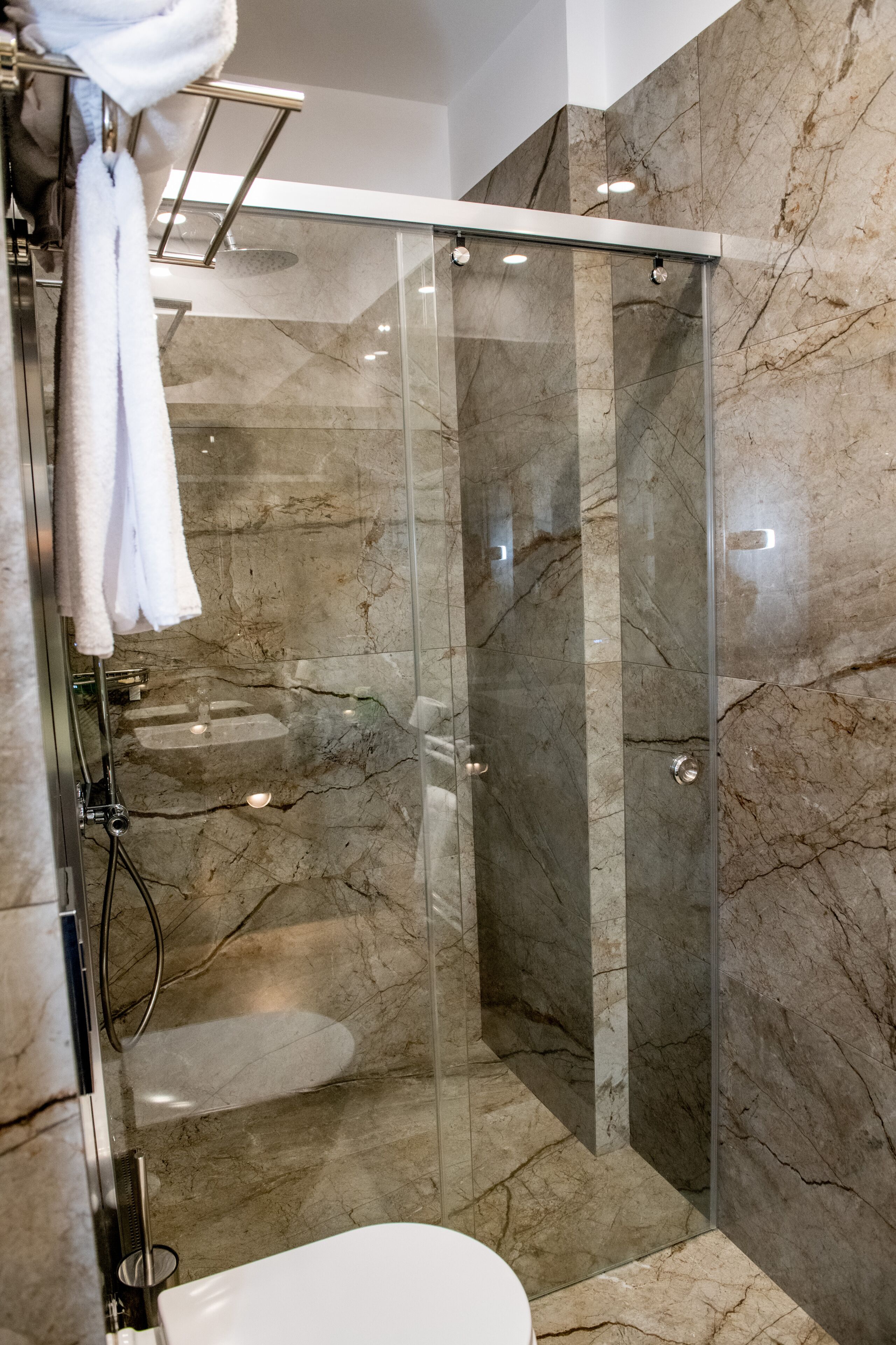 A modern bathroom with a glass-enclosed shower, marble walls, and a white toilet.