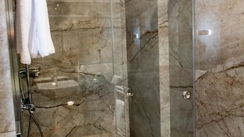 A modern bathroom with a glass-enclosed shower, marble walls, and a white toilet.