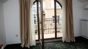 Una habitación con un amplio ventanal de arco, cortinas color beige, un radiador y una alfombra estampada.