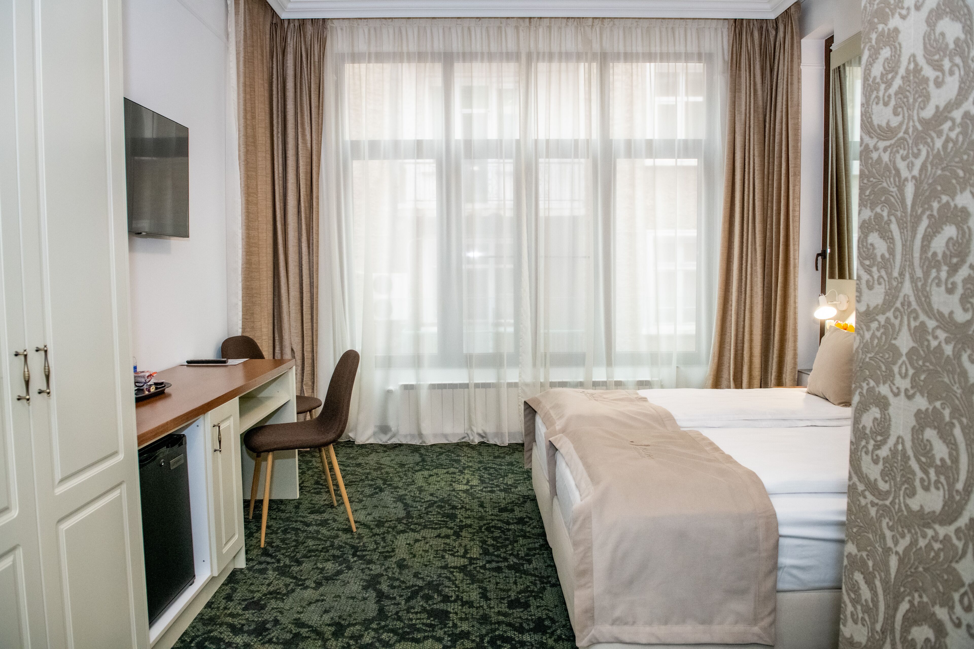 A hotel room with a bed, a desk, a chair, a television, and a window with curtains.