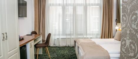 A hotel room with a bed, a desk, a chair, a television, and a window with curtains.