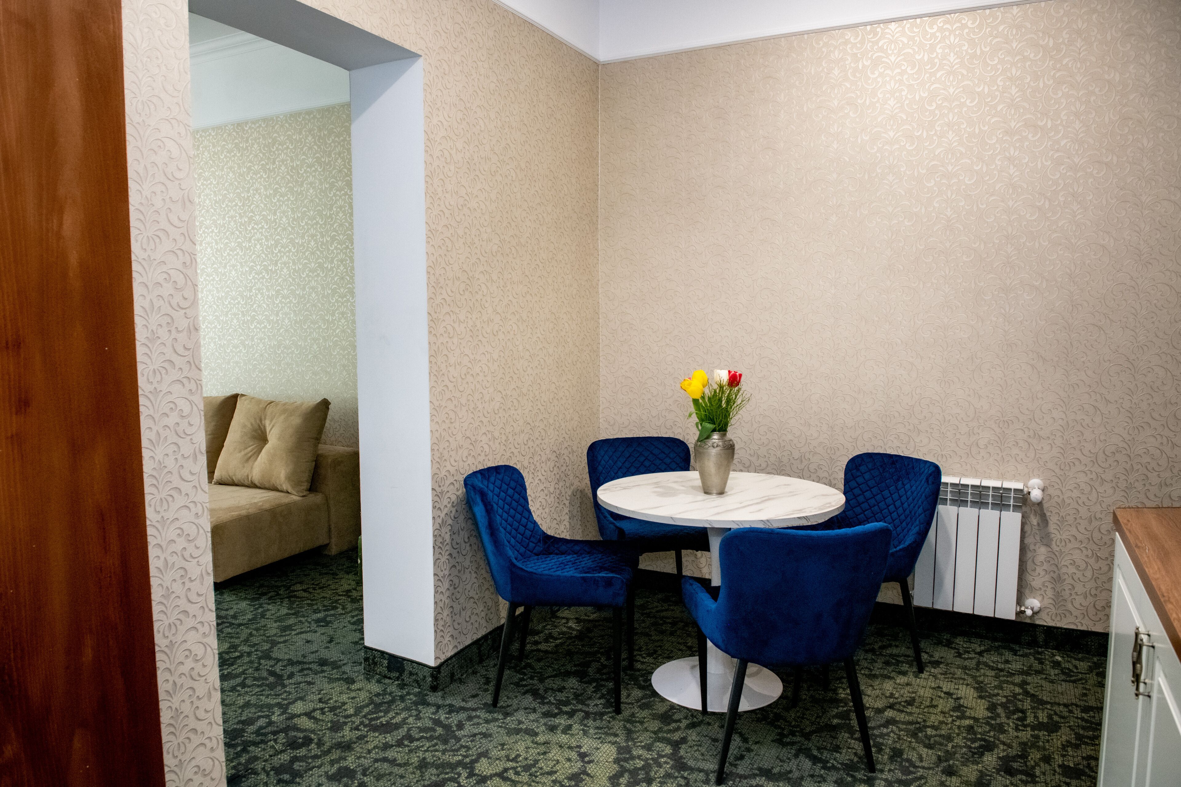 A room with a round table, blue chairs, a beige sofa, and a vase with flowers.