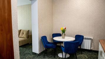 A room with a round table, blue chairs, a beige sofa, and a vase with flowers.