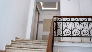 Una escalera con una lámpara circular en el techo, barandilla de metal y una puerta con el símbolo de número.