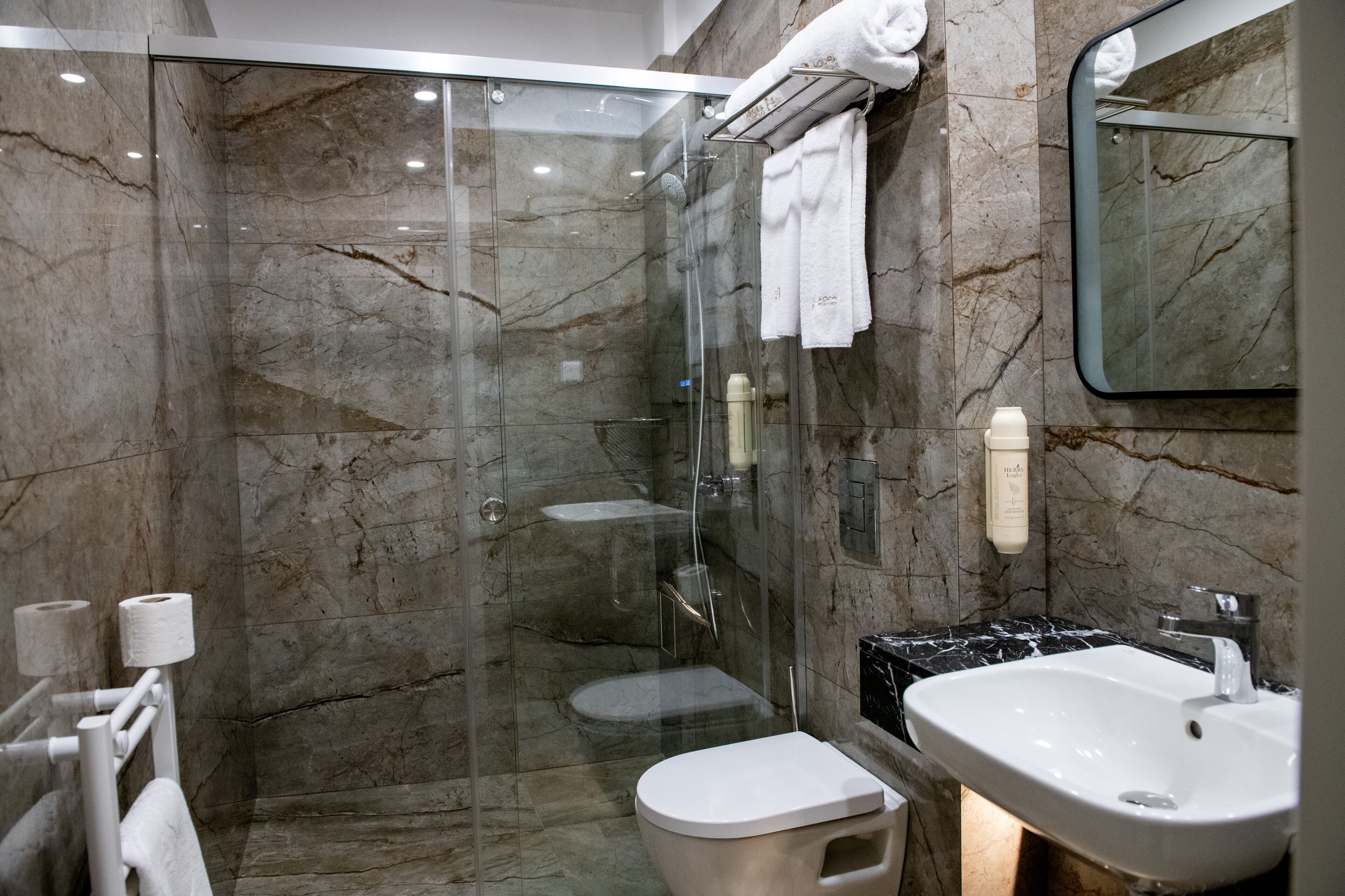 A modern bathroom with a glass-enclosed shower, a white toilet, a sink, and marble walls.