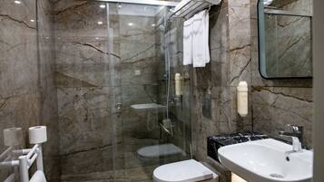 A modern bathroom with a glass-enclosed shower, a white toilet, a sink, and marble walls.