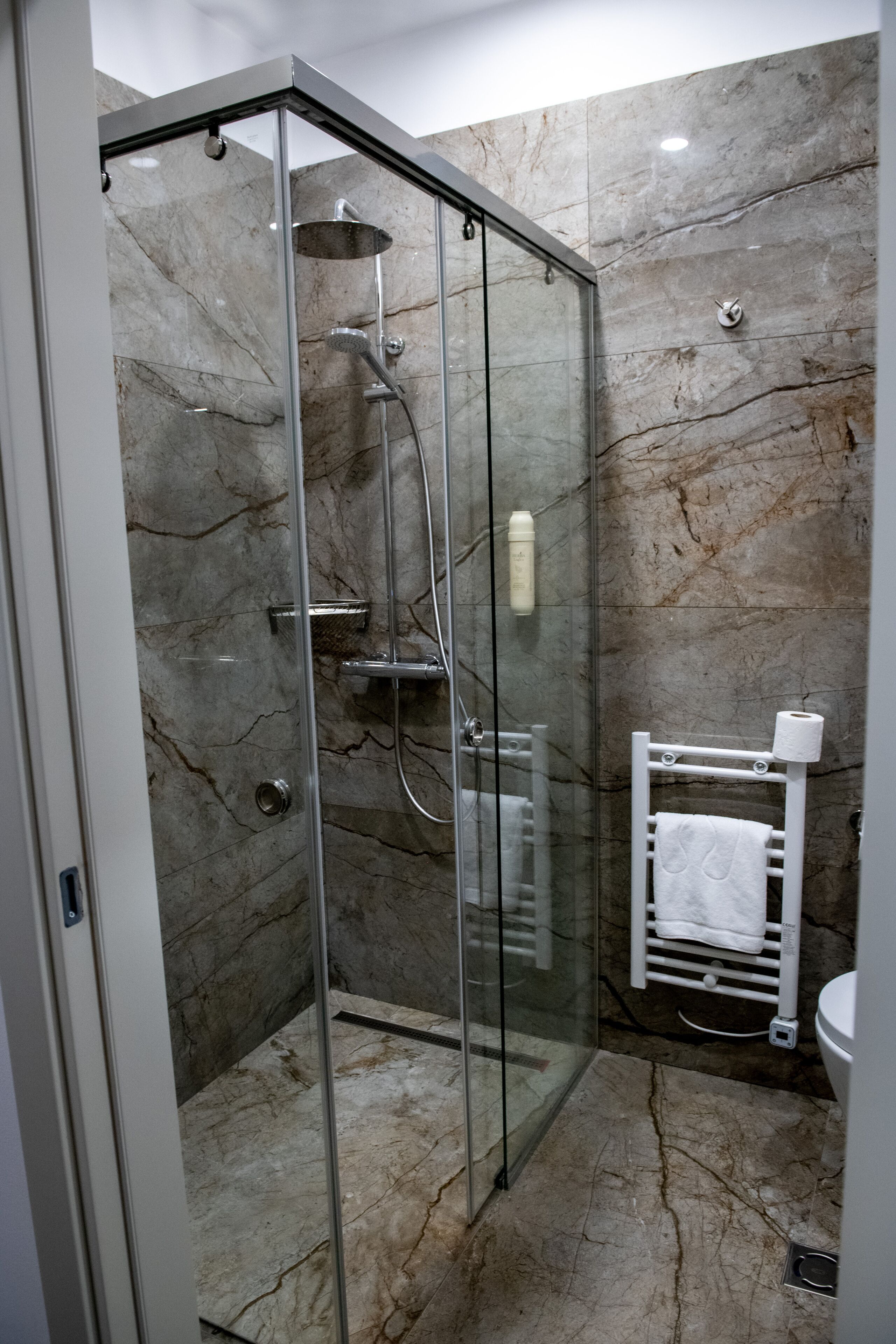 A modern bathroom with a glass-enclosed shower, marble walls, and a white towel rack.