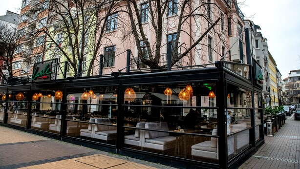 Un restaurante con terraza, grandes ventanales y luces colgantes.