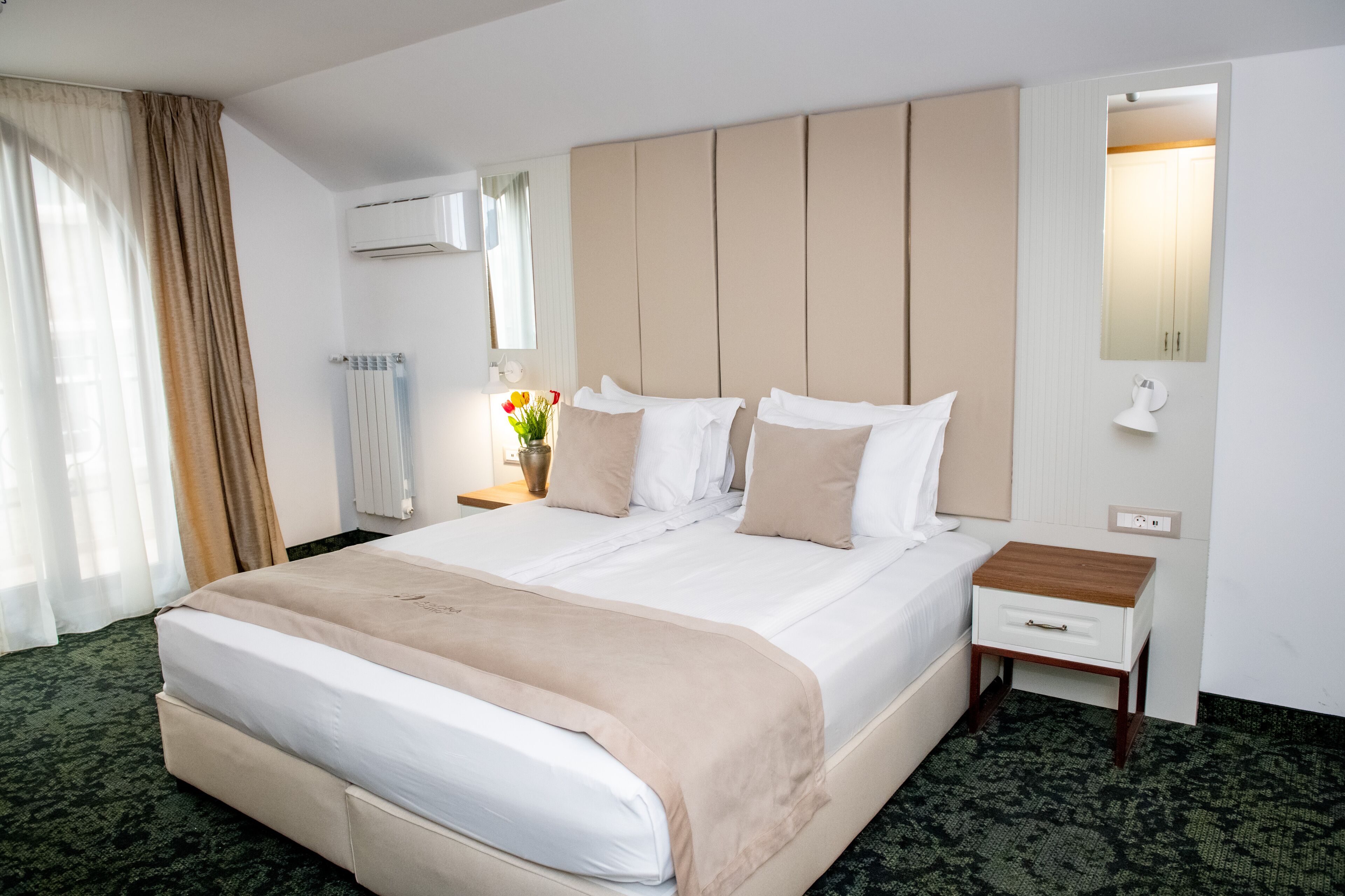 A hotel room with a large bed, a bedside table, a lamp, and a mirror.