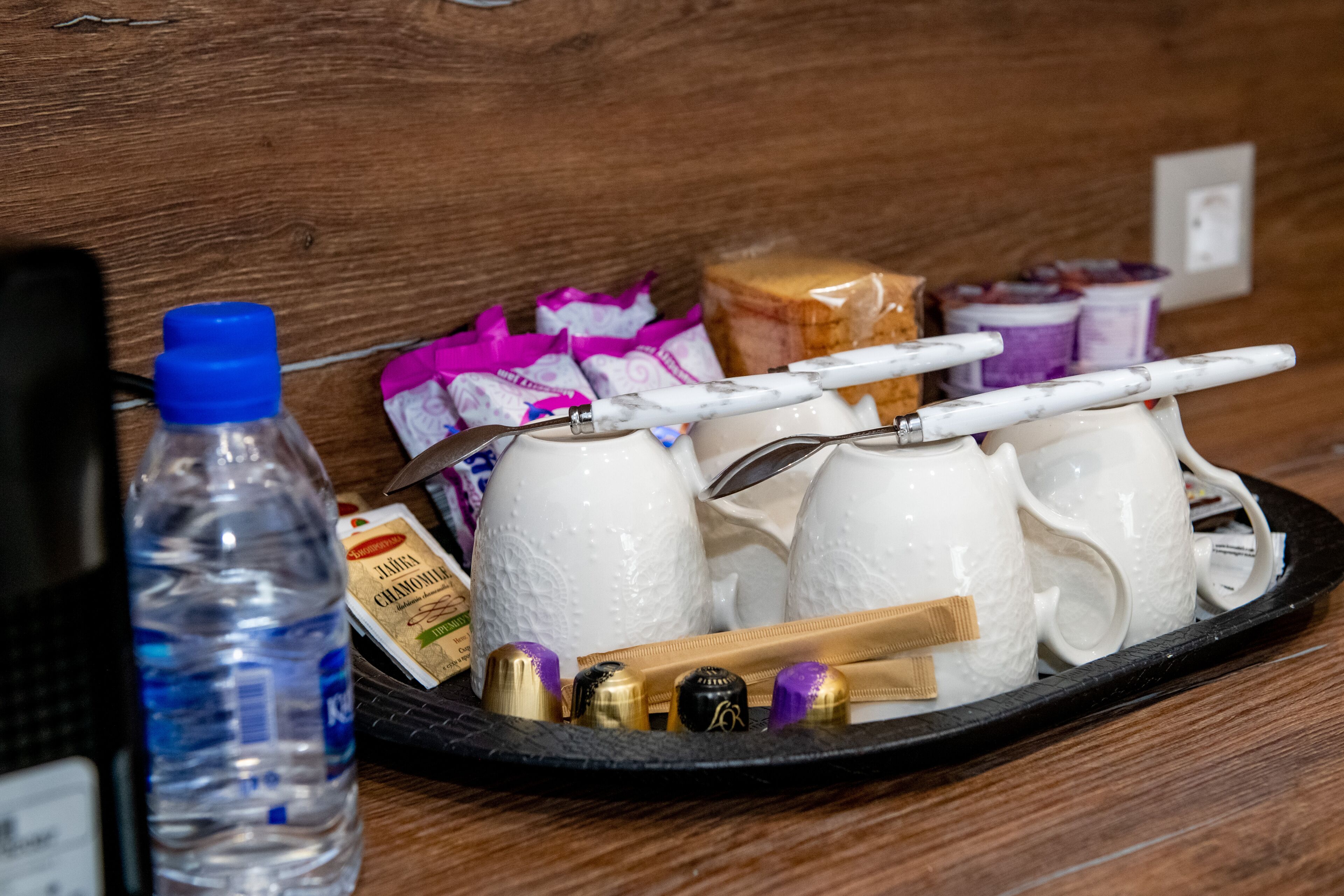 Un vassoio con tazze bianche, una bottiglia d'acqua e alcuni snack confezionati su un piano di legno.