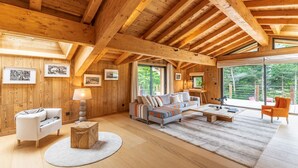 Ein geräumiges Wohnzimmer mit Holzbalken, einer Couch, einem Couchtisch und Blick ins Freie.