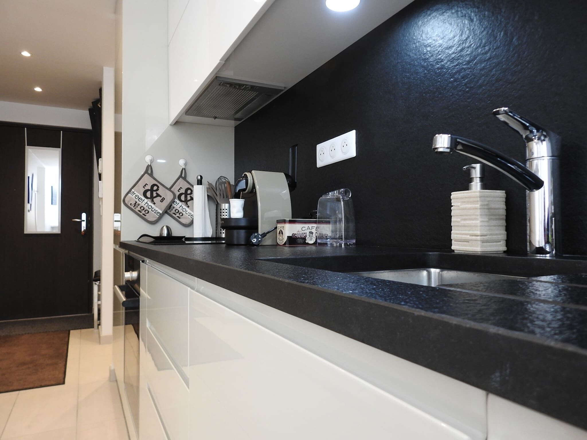 Una cocina moderna con encimera negra, pileta de acero inoxidable y cafetera.
