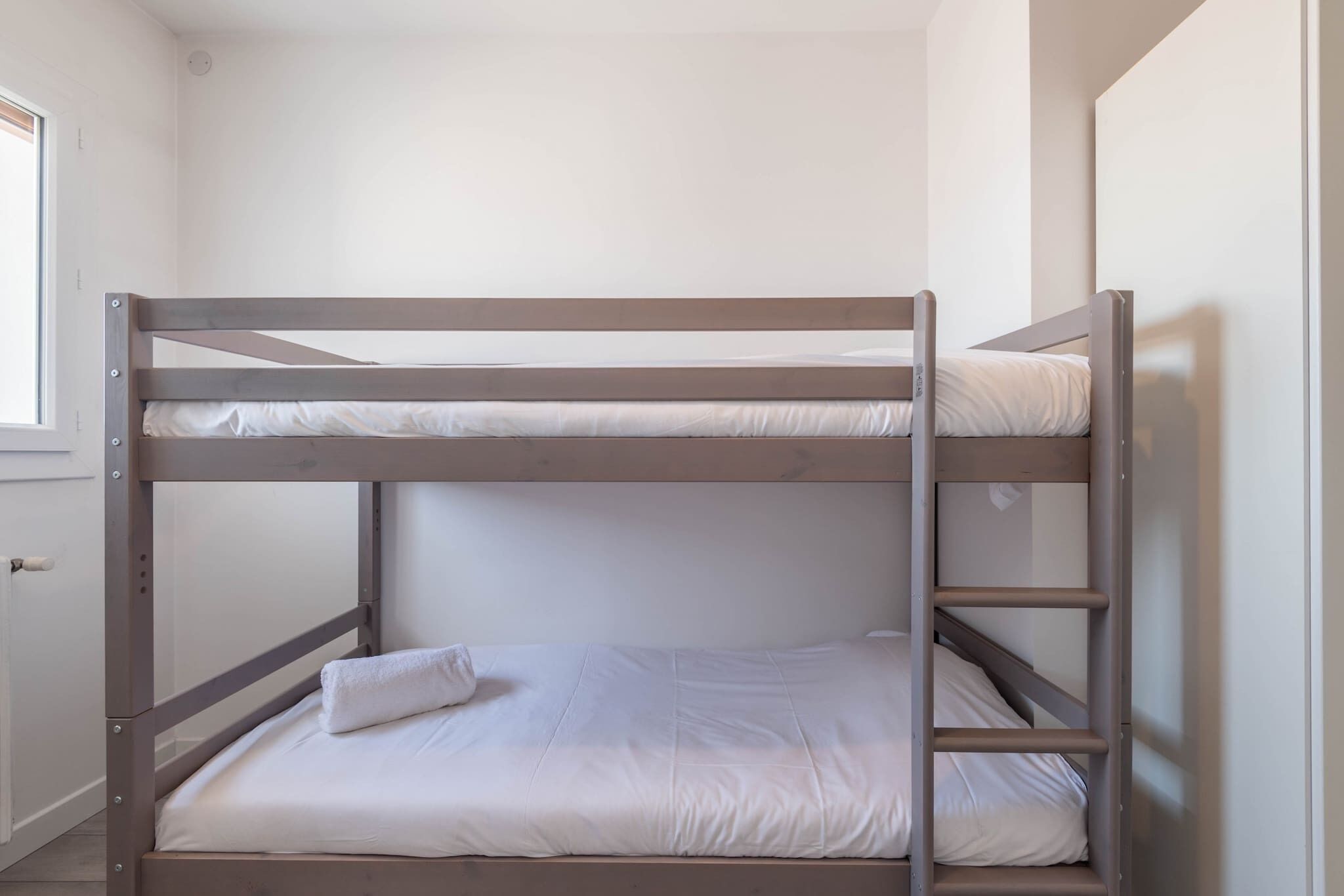 A bunk bed with two levels, a window on the left, and a door on the right.
