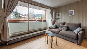 A cozy living room with a sofa, two small tables, a radiator, and a large window with curtains. - SmartStay Grand Soleil - Courchevel 1650 (Courchevel)