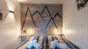 A hotel room with a wooden wall design, a bed with striped bedding, and two bedside lamps. - SmartStay Grand Soleil - Courchevel 1650 (Courchevel)