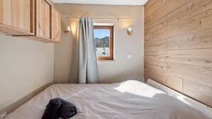A bedroom with a bed, a window with a view, wooden walls, and a curtain. - Smartstay Altineige - Val Thorens (Val-Thorens)