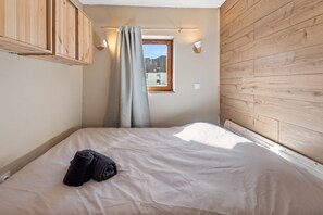 A bedroom with a bed, a window with a view, wooden walls, and a curtain. - Smartstay Altineige - Val Thorens (Val-Thorens)