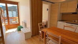 A compact kitchen with wooden cabinets, a dining table, and chairs. There is a small white refrigerator and a wooden bench near the window. - Smartstay Altineige - Val Thorens (Val-Thorens)