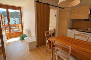 A compact kitchen with wooden cabinets, a dining table, and chairs. There is a small white refrigerator and a wooden bench near the window. - Smartstay Altineige - Val Thorens (Val-Thorens)