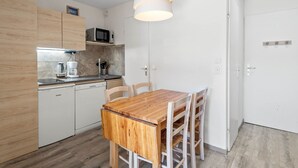 A compact kitchen with wooden cabinets, a microwave, and a dining table with chairs. - Smartstay Altineige - Val Thorens (Val-Thorens)