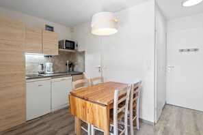 A compact kitchen with wooden cabinets, a microwave, and a dining table with chairs. - Smartstay Altineige - Val Thorens (Val-Thorens)