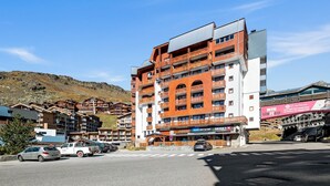 A multi-story hotel with balconies, a ski shop, and a view of the surrounding mountainous area. - Smartstay Altineige - Val Thorens (Val-Thorens)