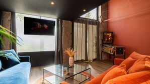 A modern living room with a blue sofa, orange sofa, glass coffee table, and a television on the wall.